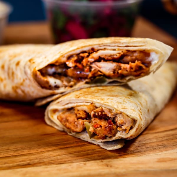 Two Mediterranean shawarma wraps, cut in half, revealing chicken and sauce on a wooden board.