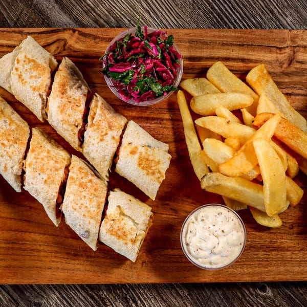 Mediterranean wraps, fries, red cabbage salad, and dipping sauce on a wooden board.
