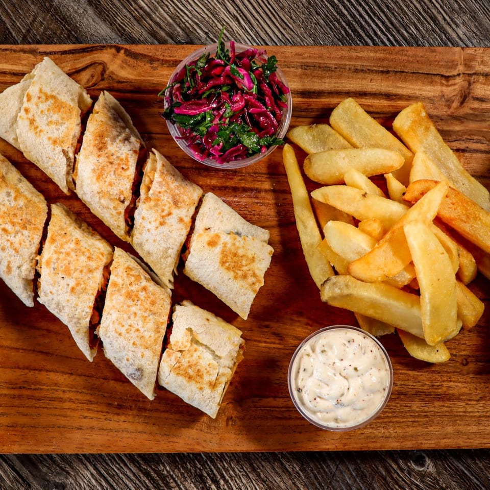 Mediterranean wraps, fries, red cabbage salad, and dipping sauce on a wooden board.