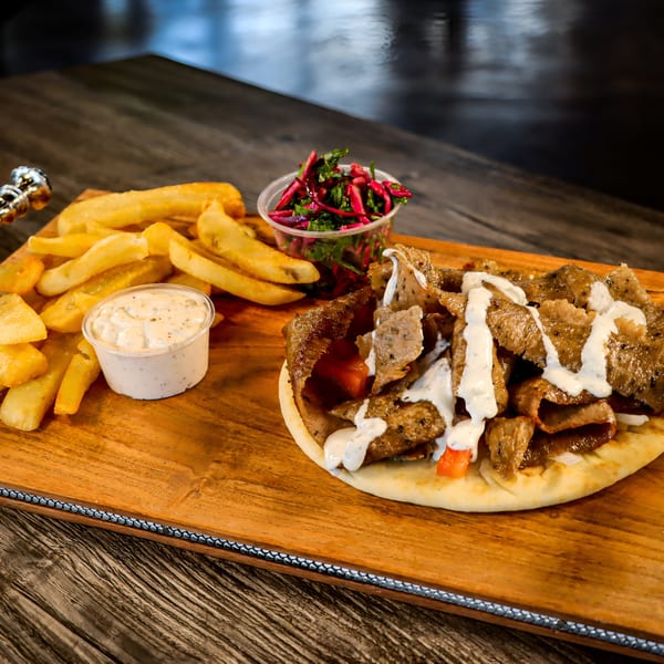 Niro's House Mediterranean Kitchen gyro with fries, dipping sauce, and a side salad on a wooden board.